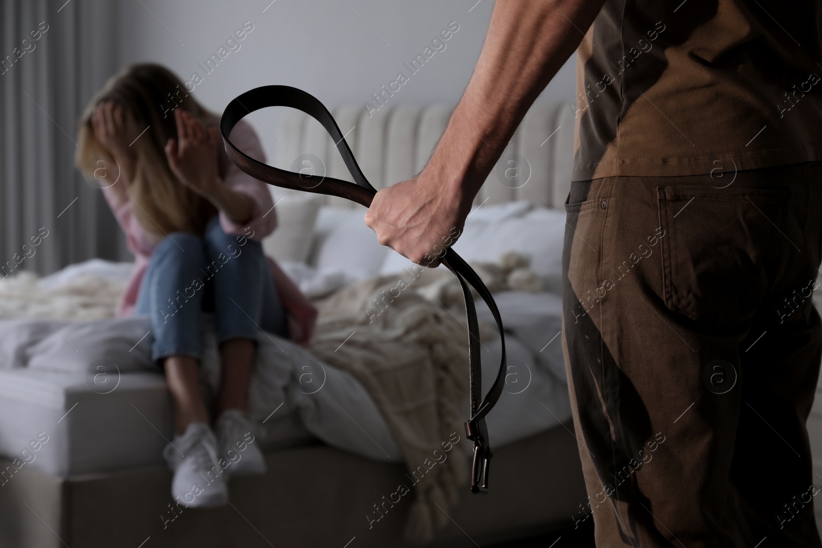 Photo of Man threatening woman with belt indoors, closeup. Domestic violence