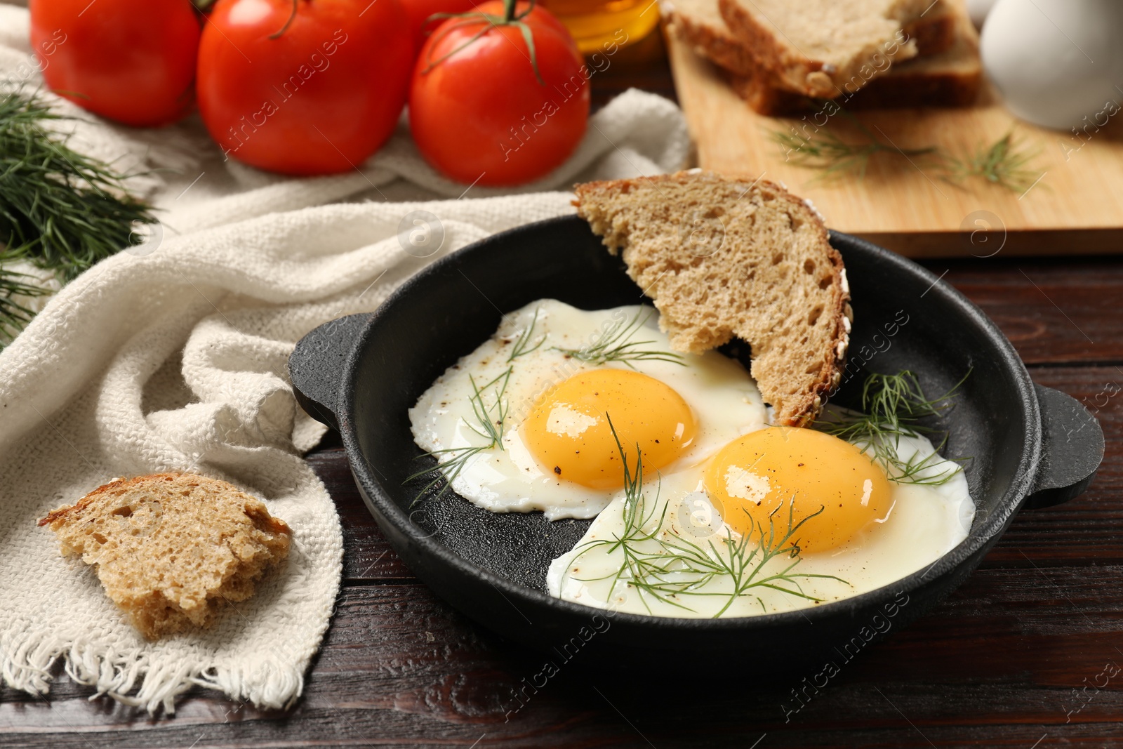 Photo of Delicious fried eggs served with bread and tomatoes on wooden table