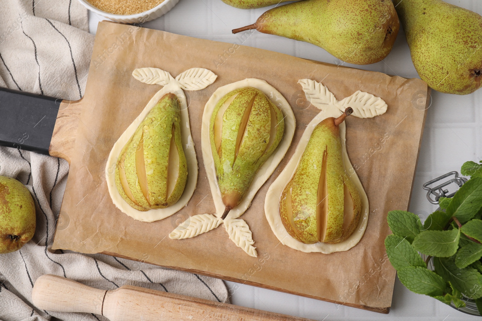 Photo of Board with raw dough, fresh pears and mint on white tiled table, flat lay