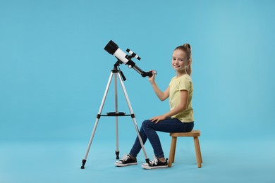 Photo of Happy little girl with telescope on light blue background
