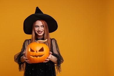 Photo of Happy young woman in scary witch costume with carved pumpkin on orange background, space for text. Halloween celebration