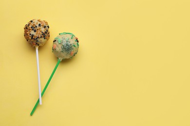 Photo of Delicious confectionery. Sweet cake pops decorated with sprinkles on pale yellow background, flat lay. Space for text