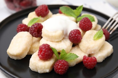 Photo of Plate of tasty lazy dumplings with raspberries, sour cream and mint leaves on table, closeup