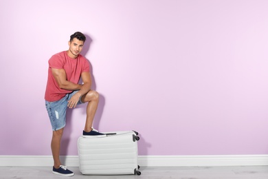 Photo of Young man with suitcase on color wall background. Space for text