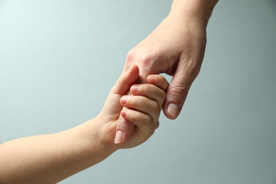 Photo of Mother and child holding hands on light blue background, closeup