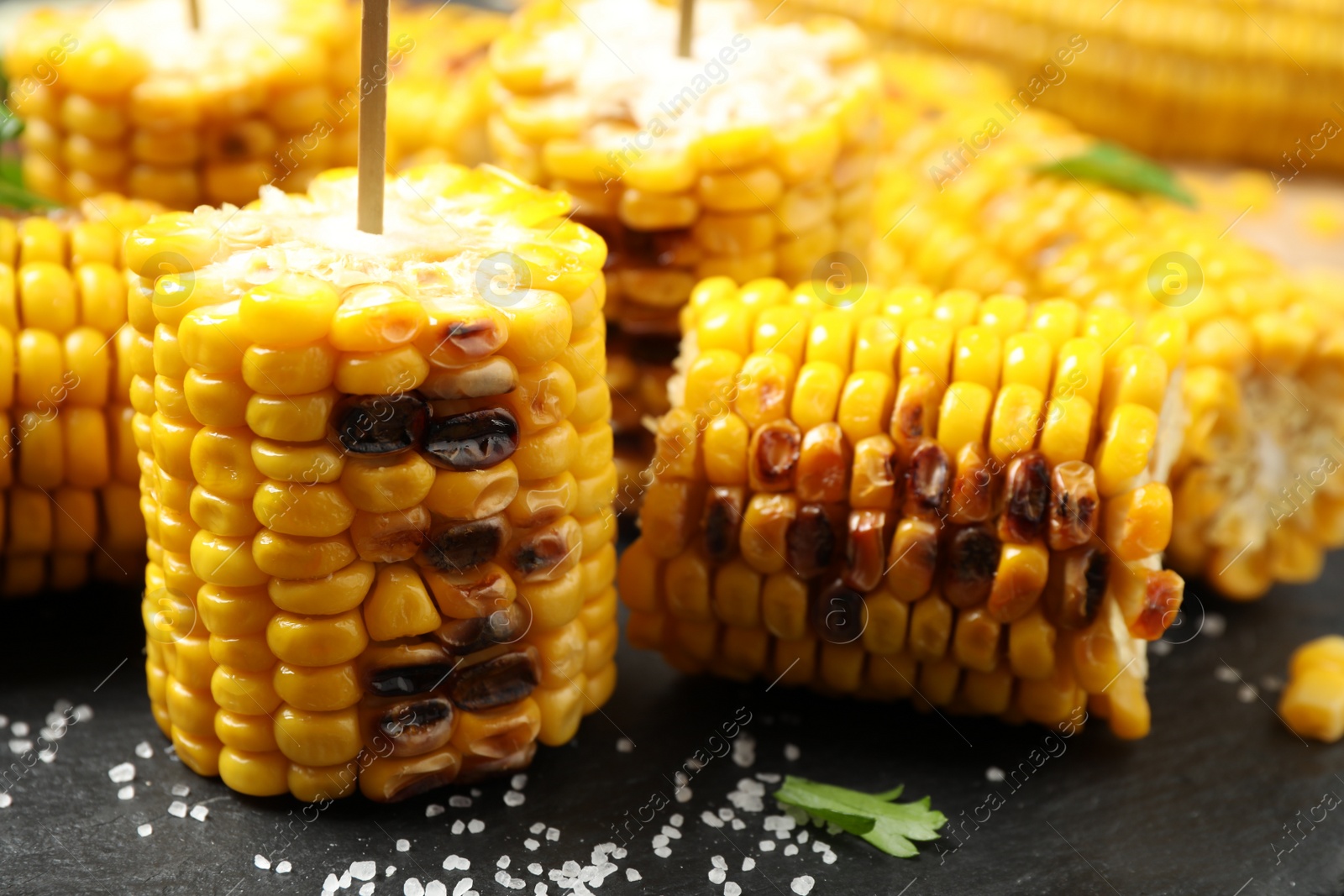 Photo of Tasty grilled corn on black plate, closeup