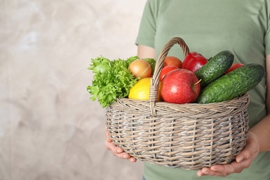 Photo of Woman holding wicker basket with ripe fruits and vegetables on color background, closeup. Space for text