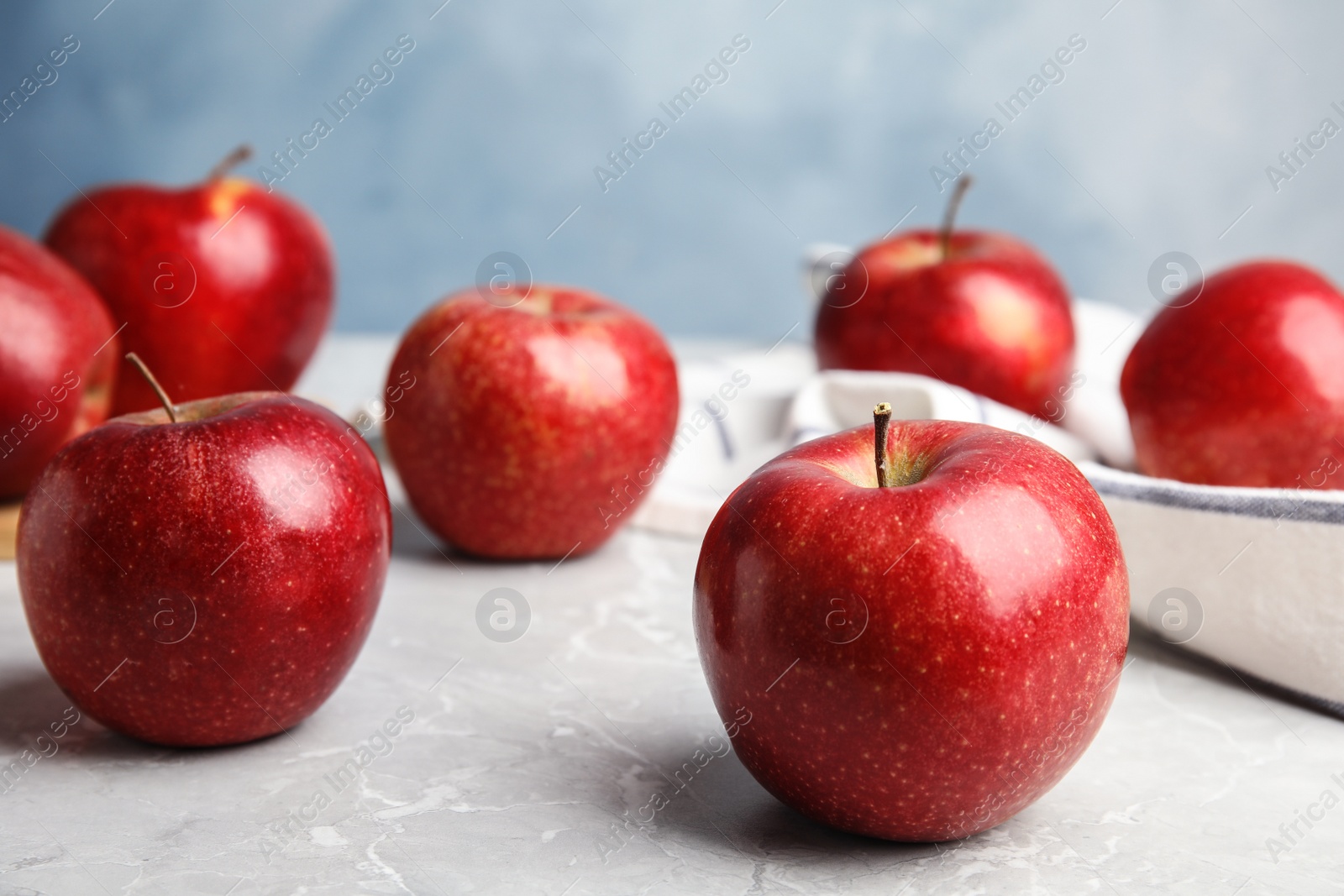 Photo of Ripe juicy red apples on grey table against blue background. Space for text