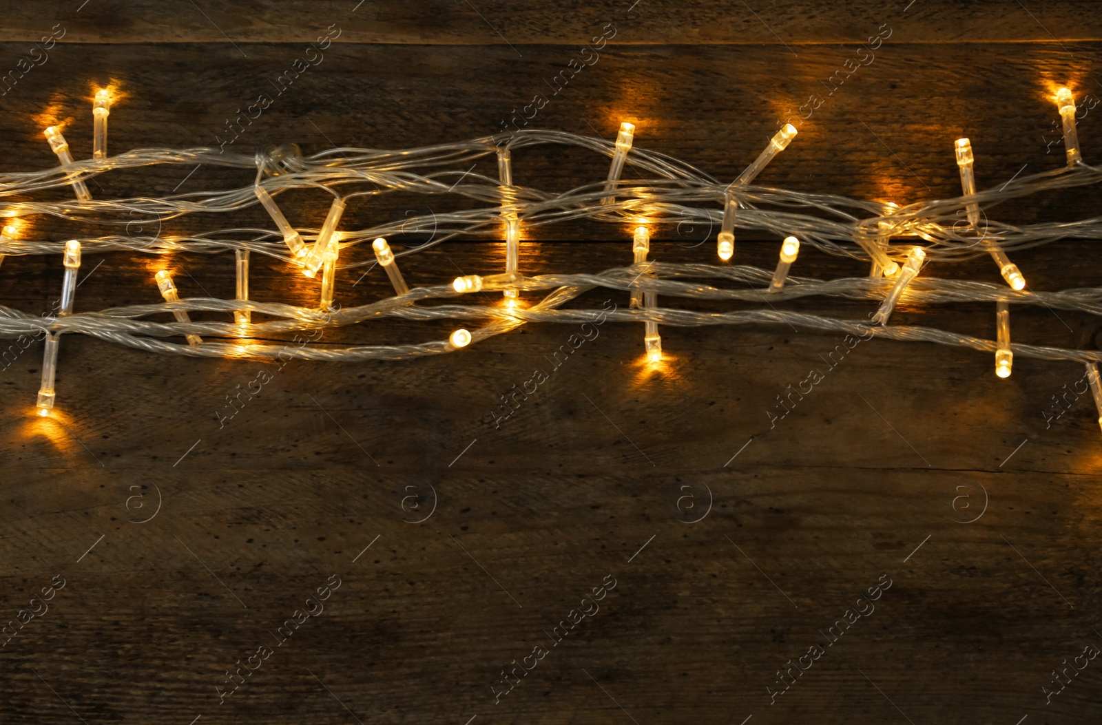 Photo of Glowing Christmas lights on wooden background, top view. Space for text