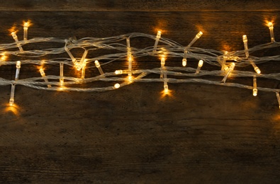 Photo of Glowing Christmas lights on wooden background, top view. Space for text