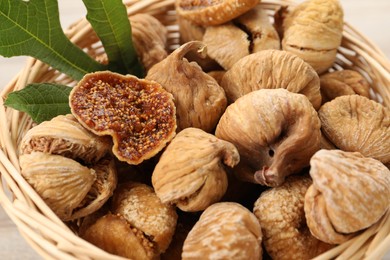 Photo of Wicker basket with tasty dried figs and green leaf on table, closeup