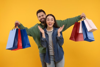 Photo of Excited couple with shopping bags on orange background