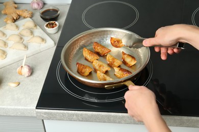 Photo of Woman cooking gyoza on frying pan with hot oil in kitchen, closeup
