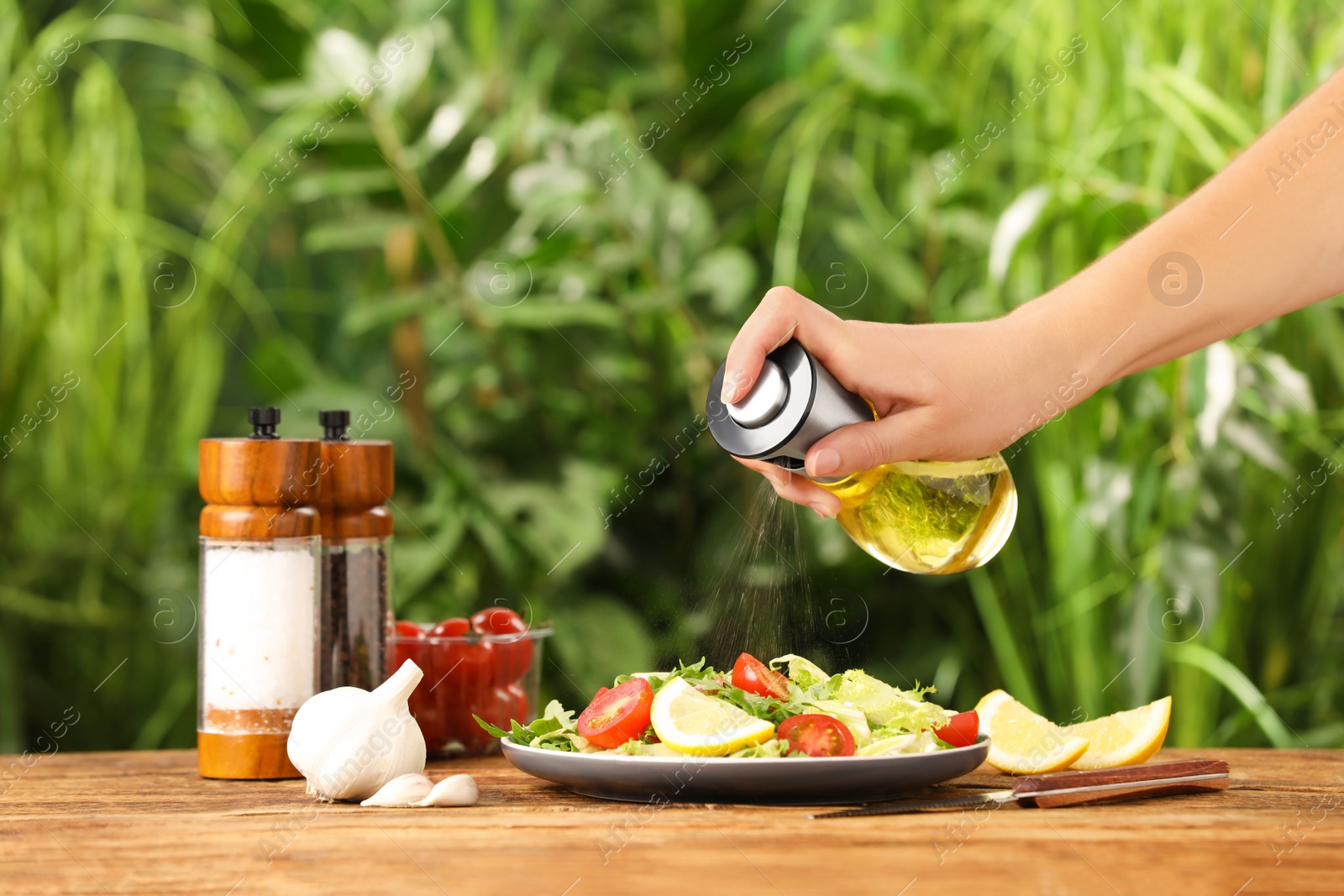 Photo of Woman dressing delicious salad with cooking oil at wooden table against blurred background, closeup