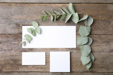 Photo of Fresh eucalyptus leaves and blank cards with space for design on wooden background, top view