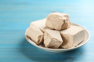 Plate with pieces of compressed yeast on light blue wooden table