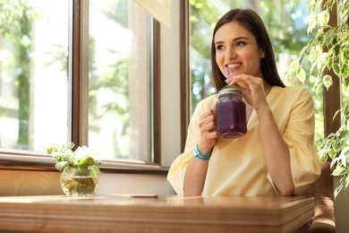 Photo of Young woman with mason jar of tasty natural lemonade in cafe. Detox drink