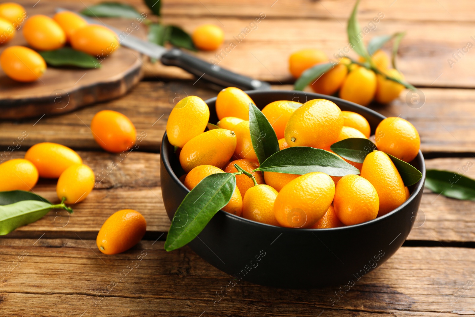 Photo of Fresh ripe kumquats in bowl on wooden table