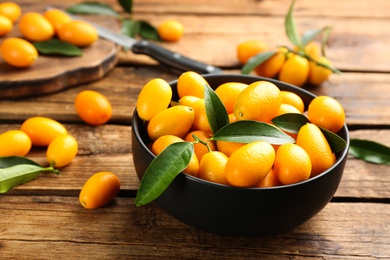 Photo of Fresh ripe kumquats in bowl on wooden table