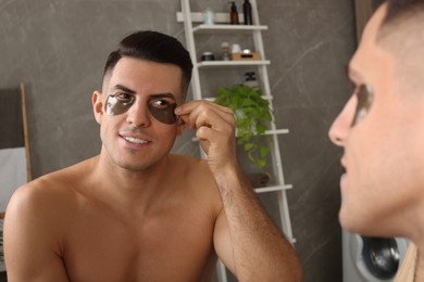 Photo of Man applying dark under eye patches near mirror at home