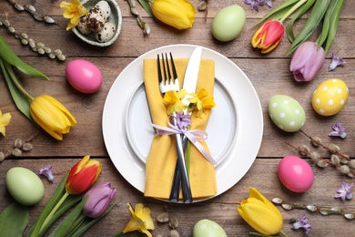 Photo of Festive Easter table setting with painted eggs and floral decor on wooden background, flat lay