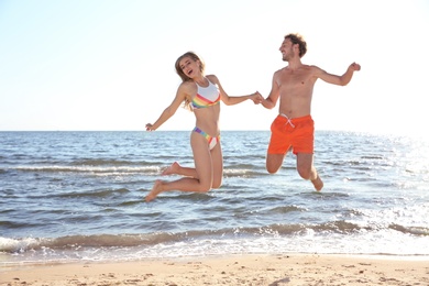 Photo of Happy young couple in beachwear jumping on seashore