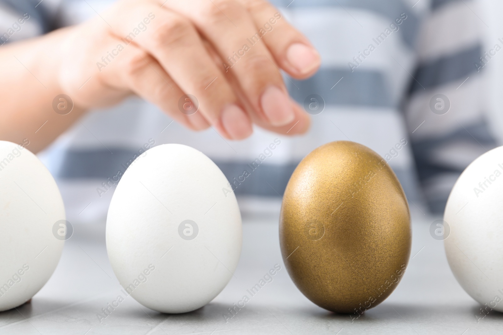 Photo of Woman choosing golden egg from white ones at table, closeup