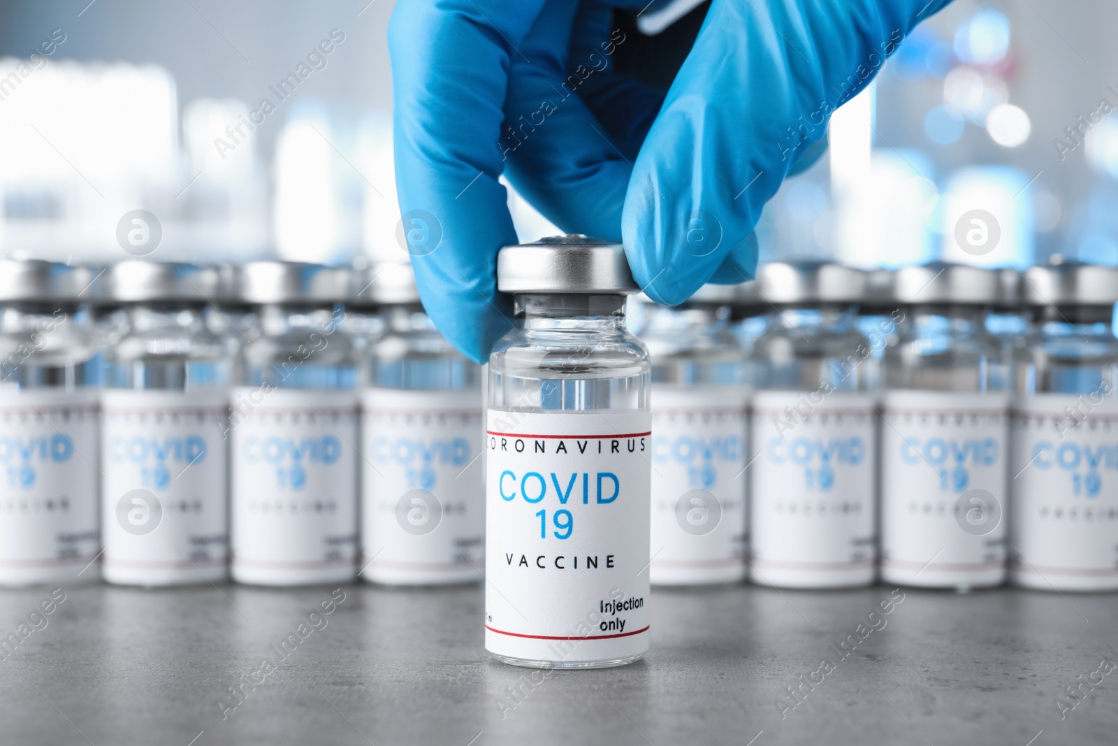 Photo of Doctor taking glass vial with COVID-19 vaccine from table, closeup