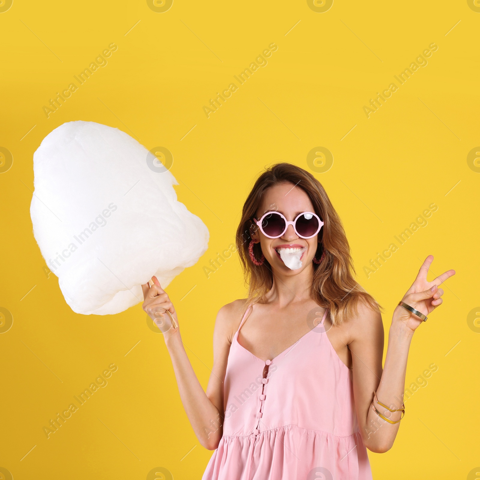 Photo of Happy young woman eating cotton candy on yellow background
