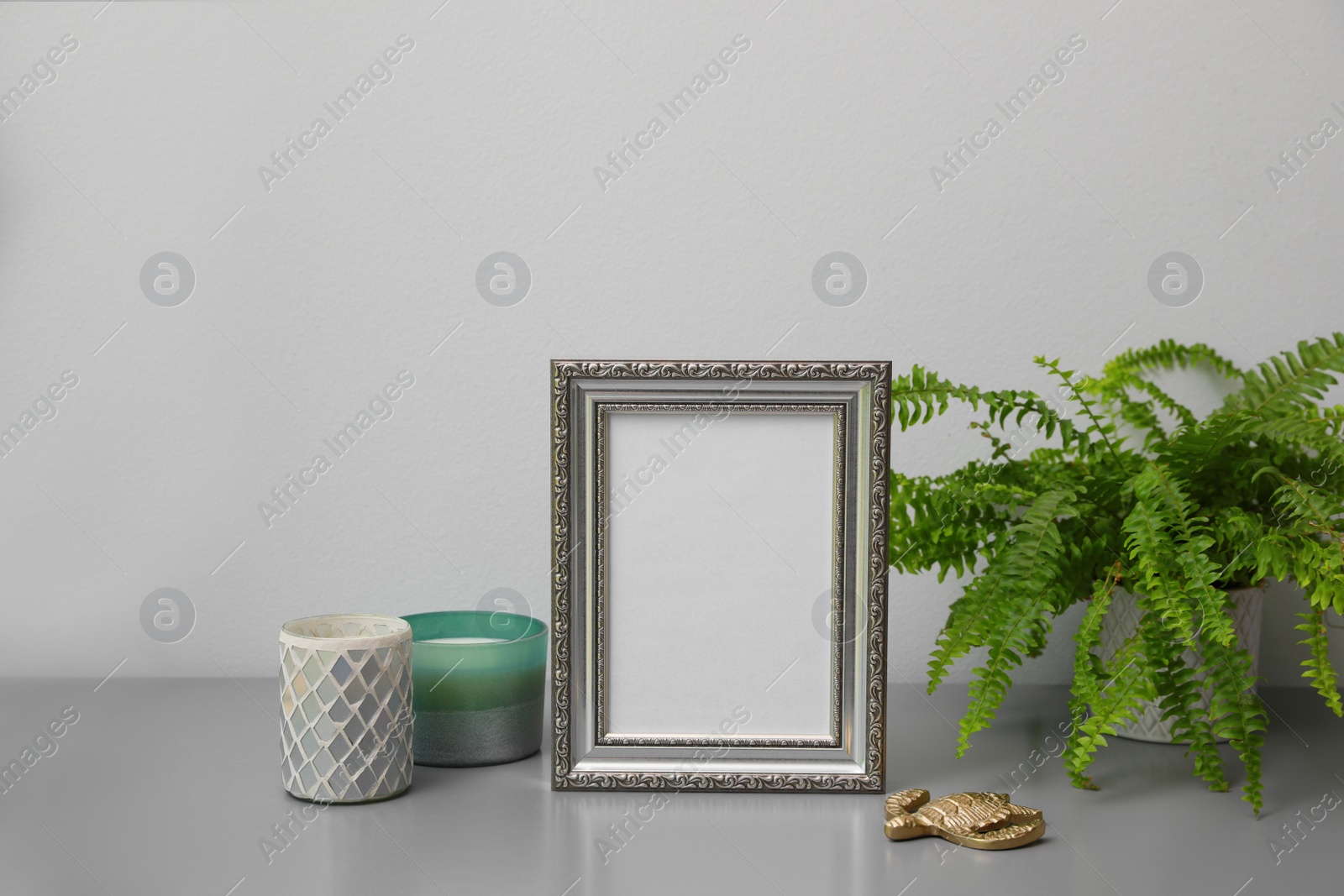 Photo of Empty photo frame, candles and green plant on grey table