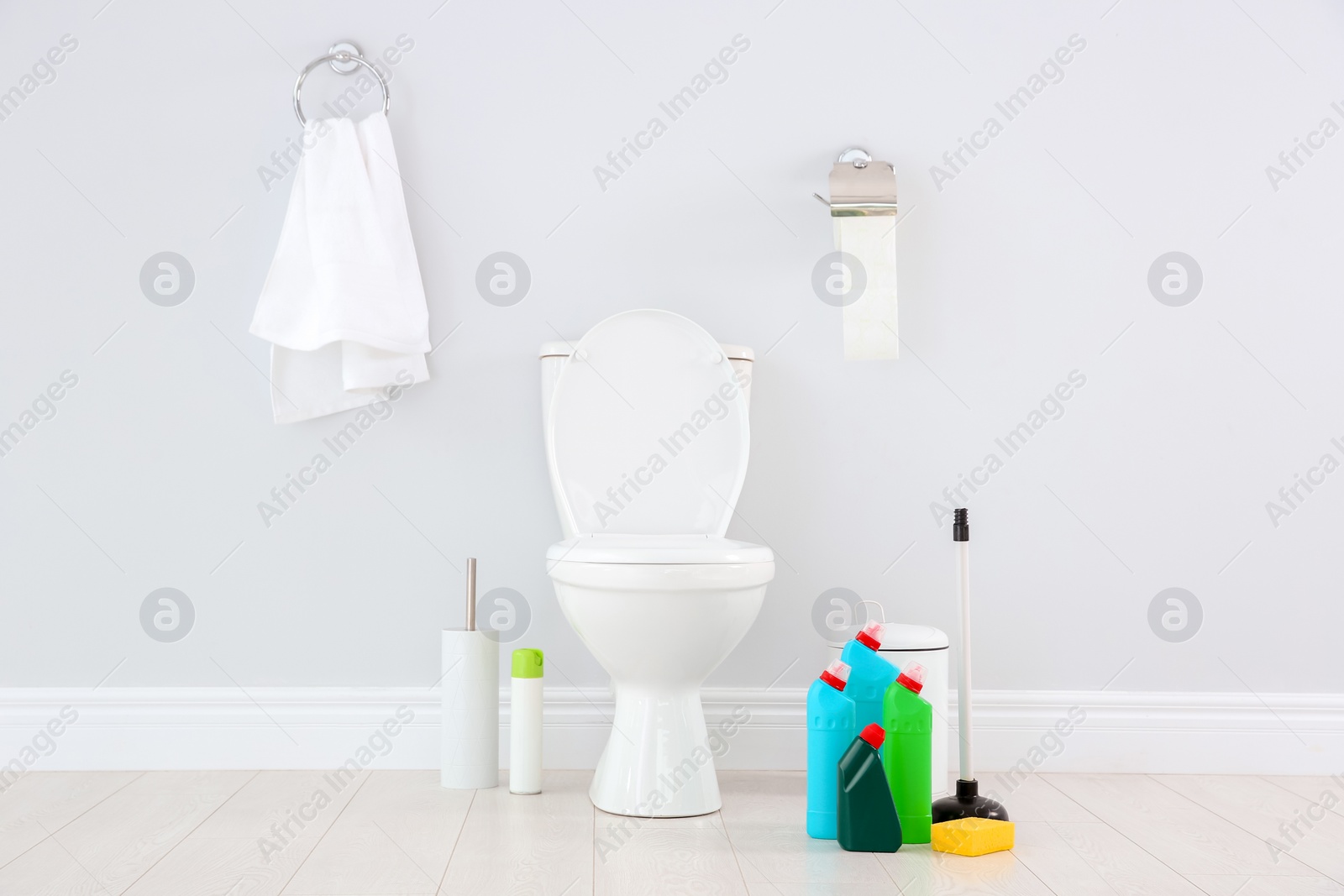 Photo of Ceramic toilet bowl, bottles of detergent and cleaning supplies in modern bathroom