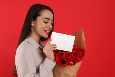 Photo of Happy woman with tulip bouquet and greeting card on red background. 8th of March celebration