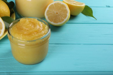 Photo of Delicious lemon curd in glass jar, fresh citrus fruits and green leaves on light blue wooden table, space for text