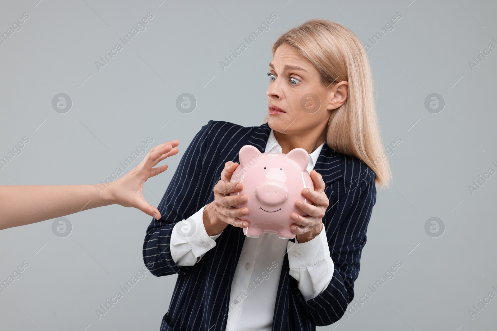 Photo of Scammer taking piggy bank from scared woman on grey background. Be careful - fraud