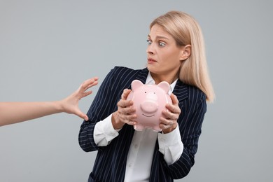 Photo of Scammer taking piggy bank from scared woman on grey background. Be careful - fraud