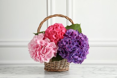 Photo of Bouquet with beautiful hortensia flowers in wicker basket on white marble table
