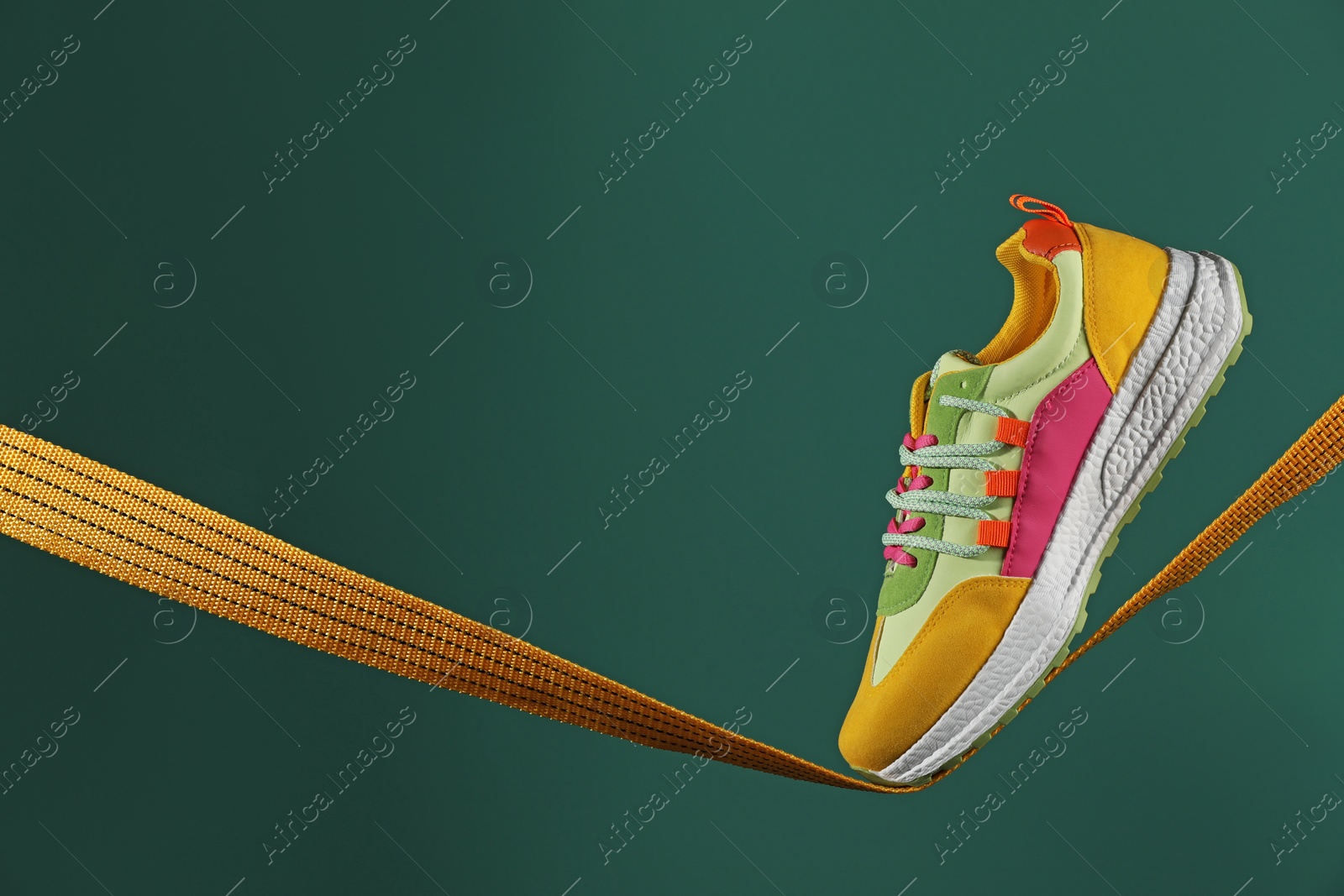 Photo of One stylish colorful sneaker on rope against green background, space for text
