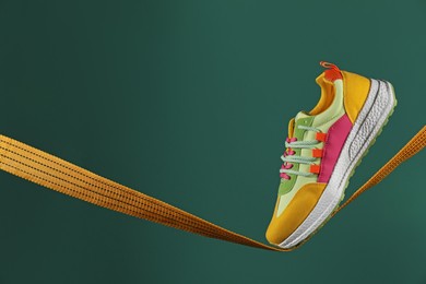 One stylish colorful sneaker on rope against green background, space for text