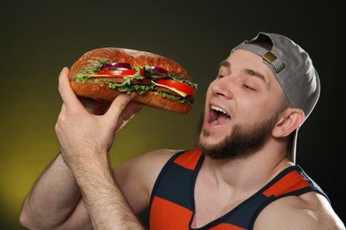 Young man eating tasty burger on color background