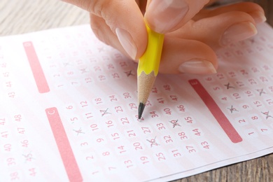 Photo of Woman filling out lottery ticket with pencil on wooden table, closeup