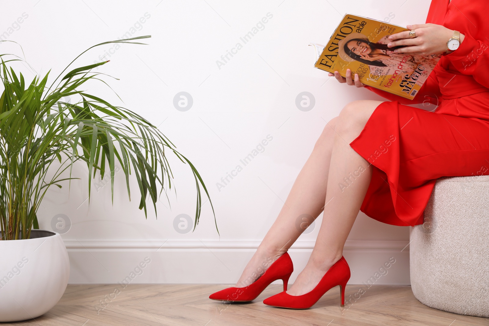 Photo of Woman reading fashion magazine near white wall indoors, closeup