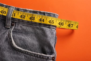 Jeans and measuring tape on orange background, top view. Weight loss concept