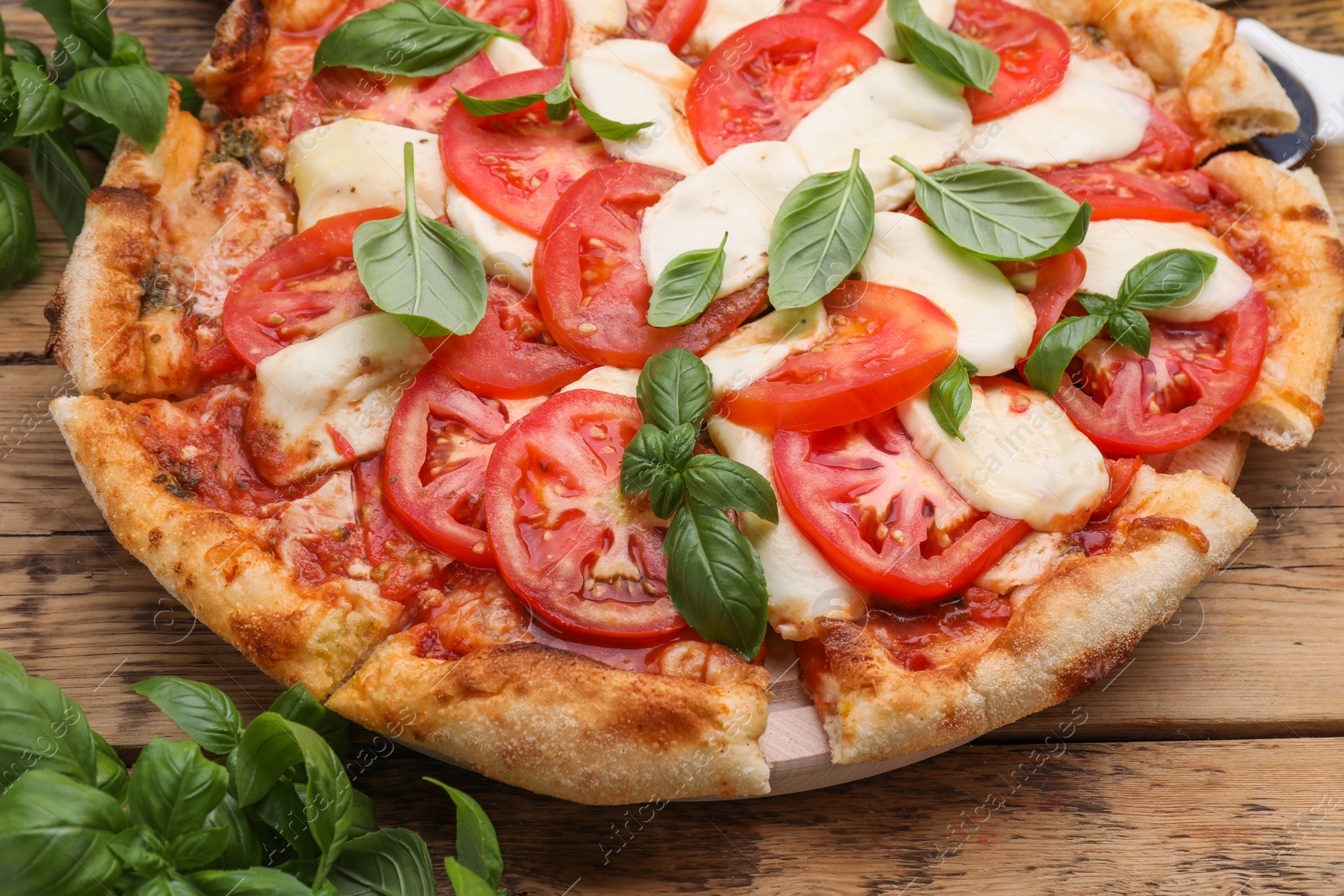 Photo of Delicious Caprese pizza with tomatoes, mozzarella and basil on wooden table, closeup