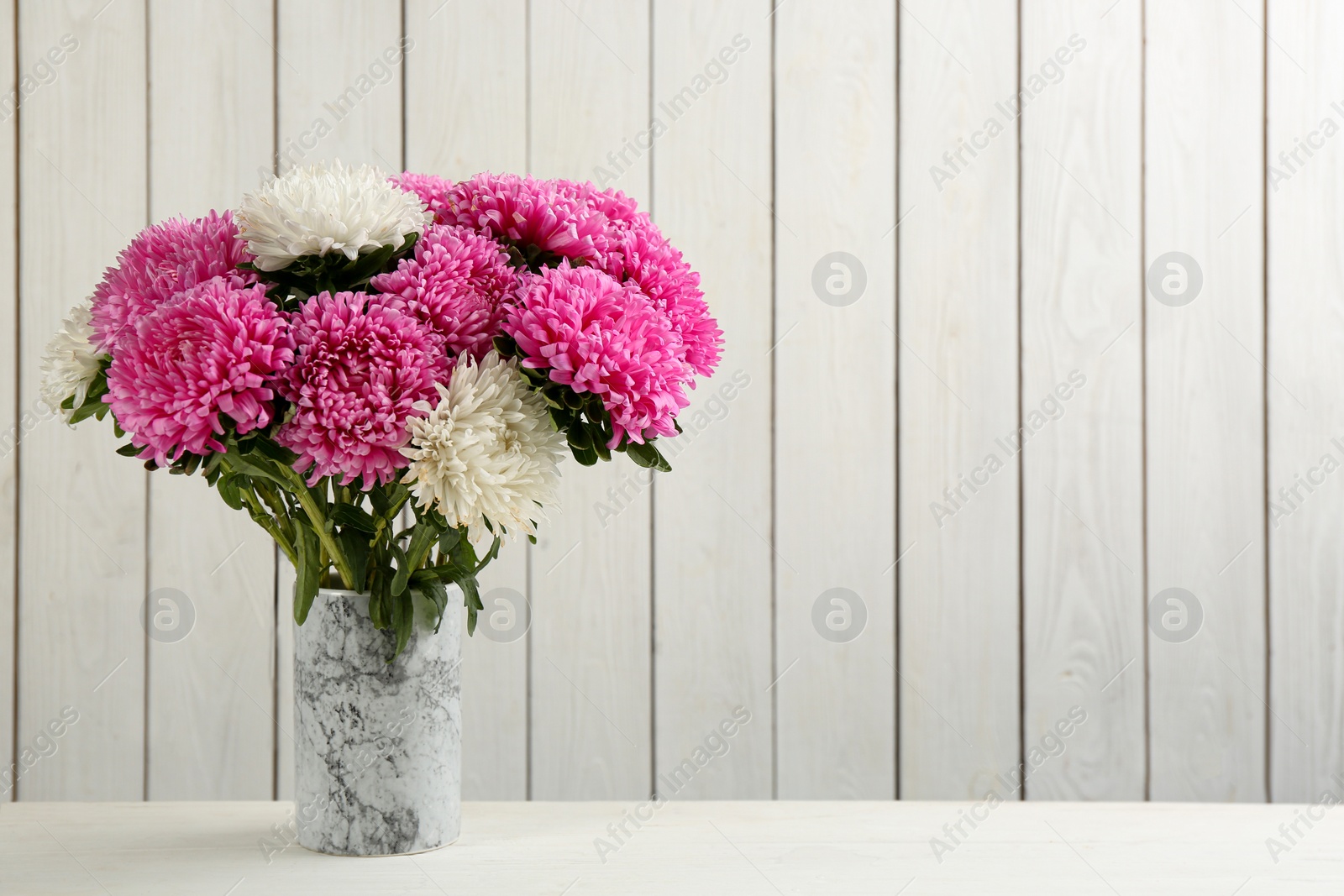 Photo of Beautiful asters in vase on table against white wooden background, space for text. Autumn flowers