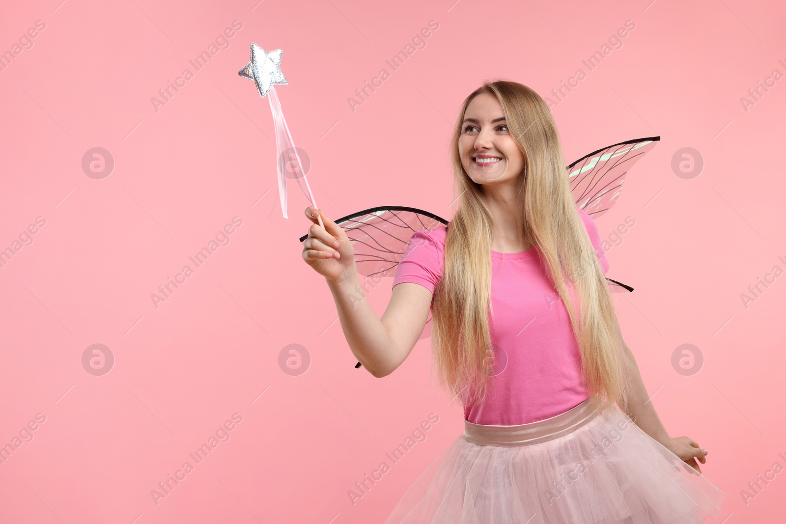 Photo of Beautiful girl in fairy costume with wings and magic wand on pink background, space for text