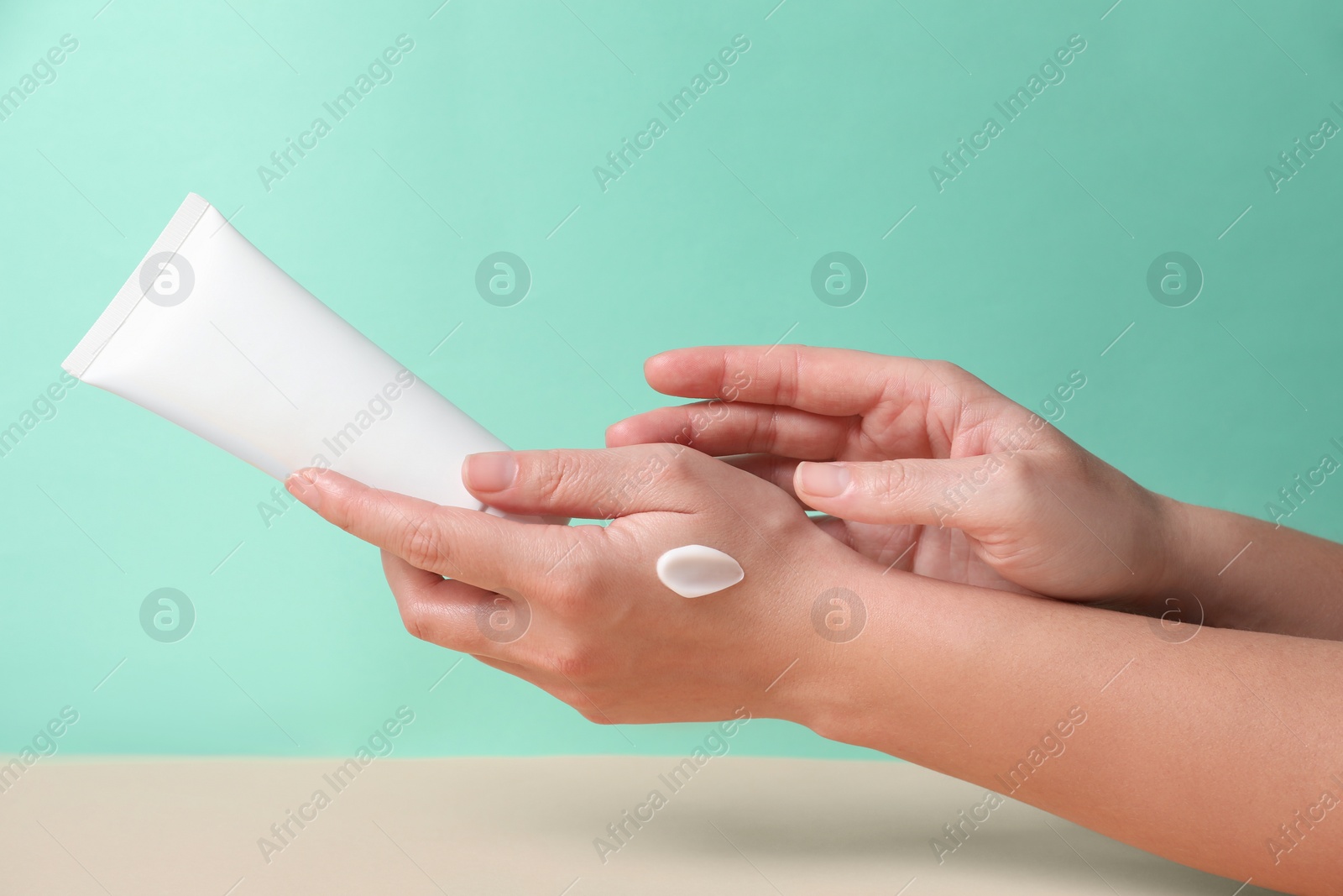 Photo of Tube of hand cream on beige table against turquoise background, closeup