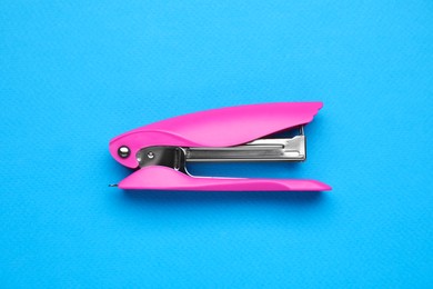 Photo of New bright stapler on light blue background, top view. School stationery