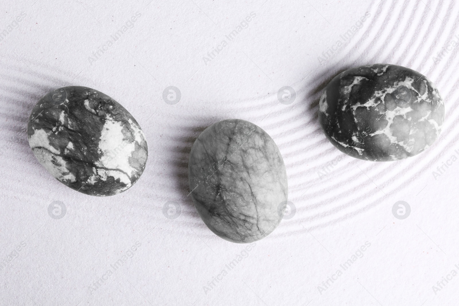 Photo of Zen garden stones on white sand with pattern, flat lay