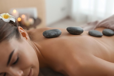 Beautiful young woman getting hot stone massage in spa salon