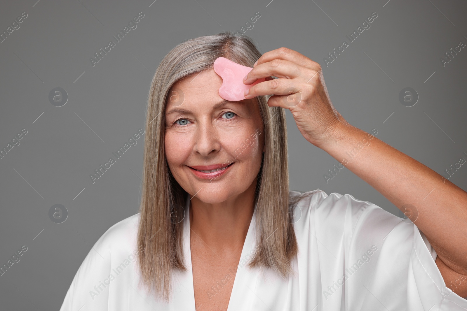 Photo of Woman massaging her face with rose quartz gua sha tool on grey background